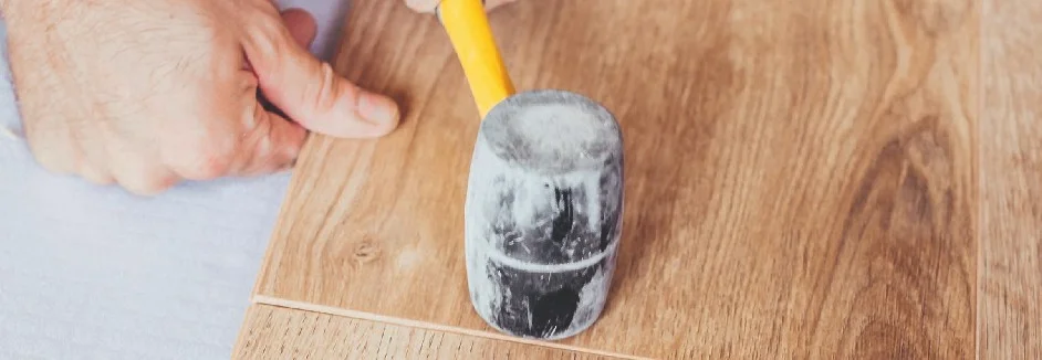 Person verlegt Holzdielen mit Gummihammer.